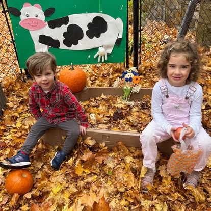 Two children sitting in autumn leaves with pumpkins and a cow cutout
