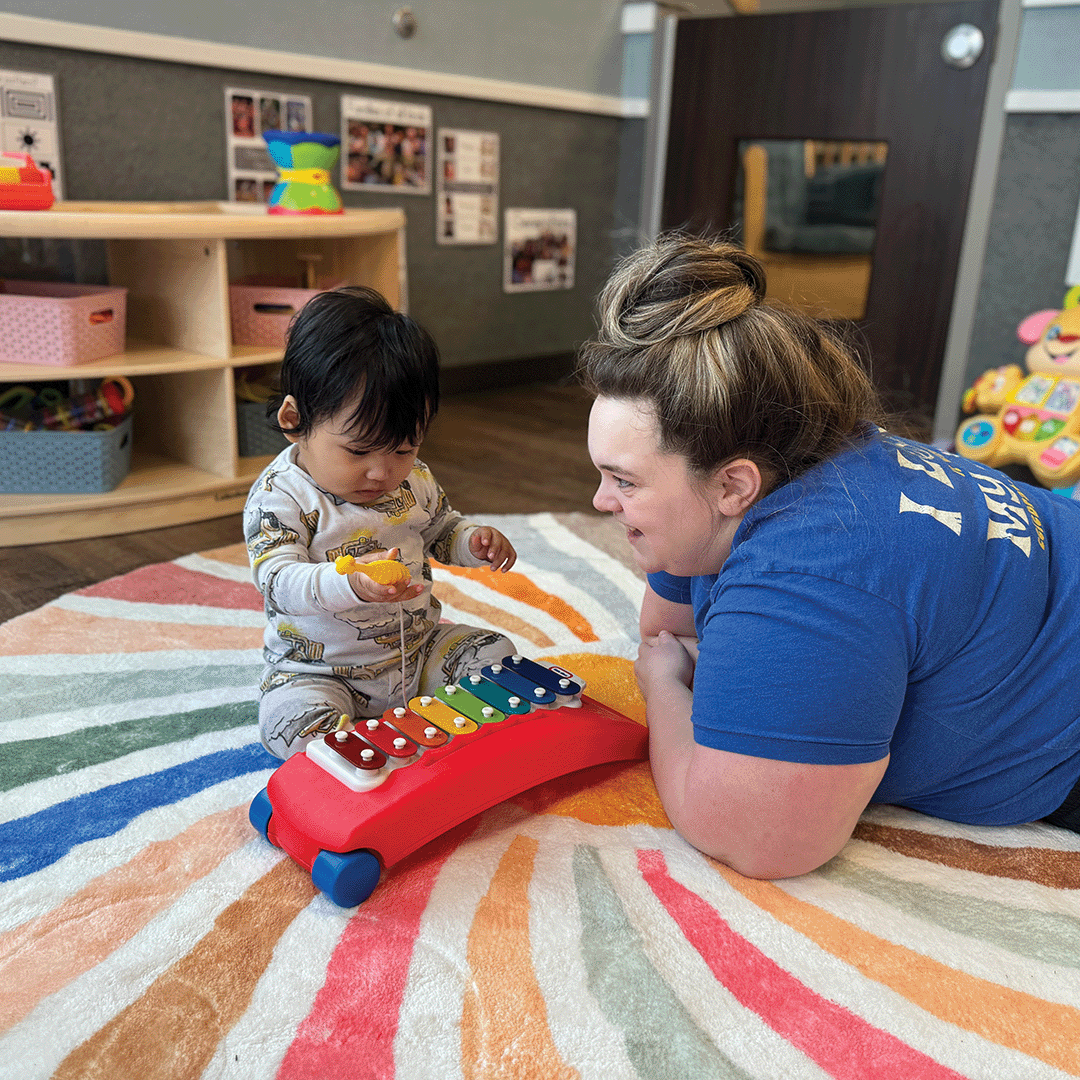 Adult and child playing with a toy xylophone on a colorful rug