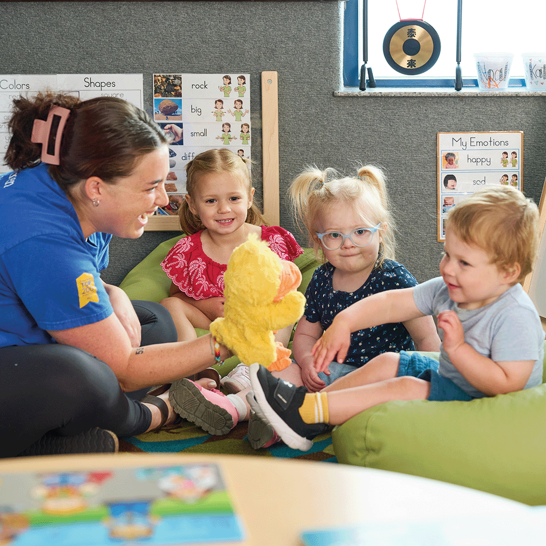 Adult and three children playing with a yellow duck puppet in a classroom