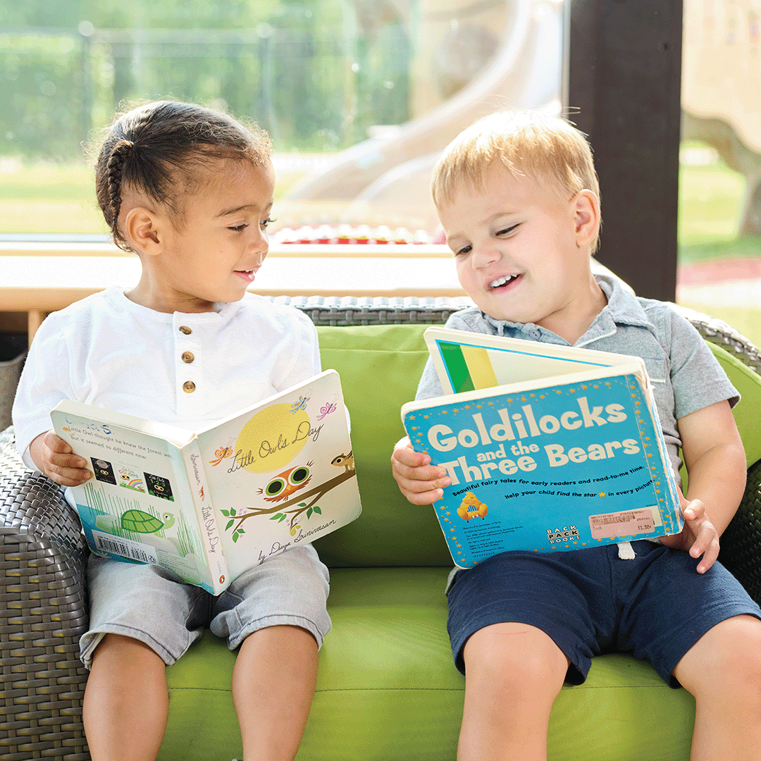 Two children sitting on a couch reading books