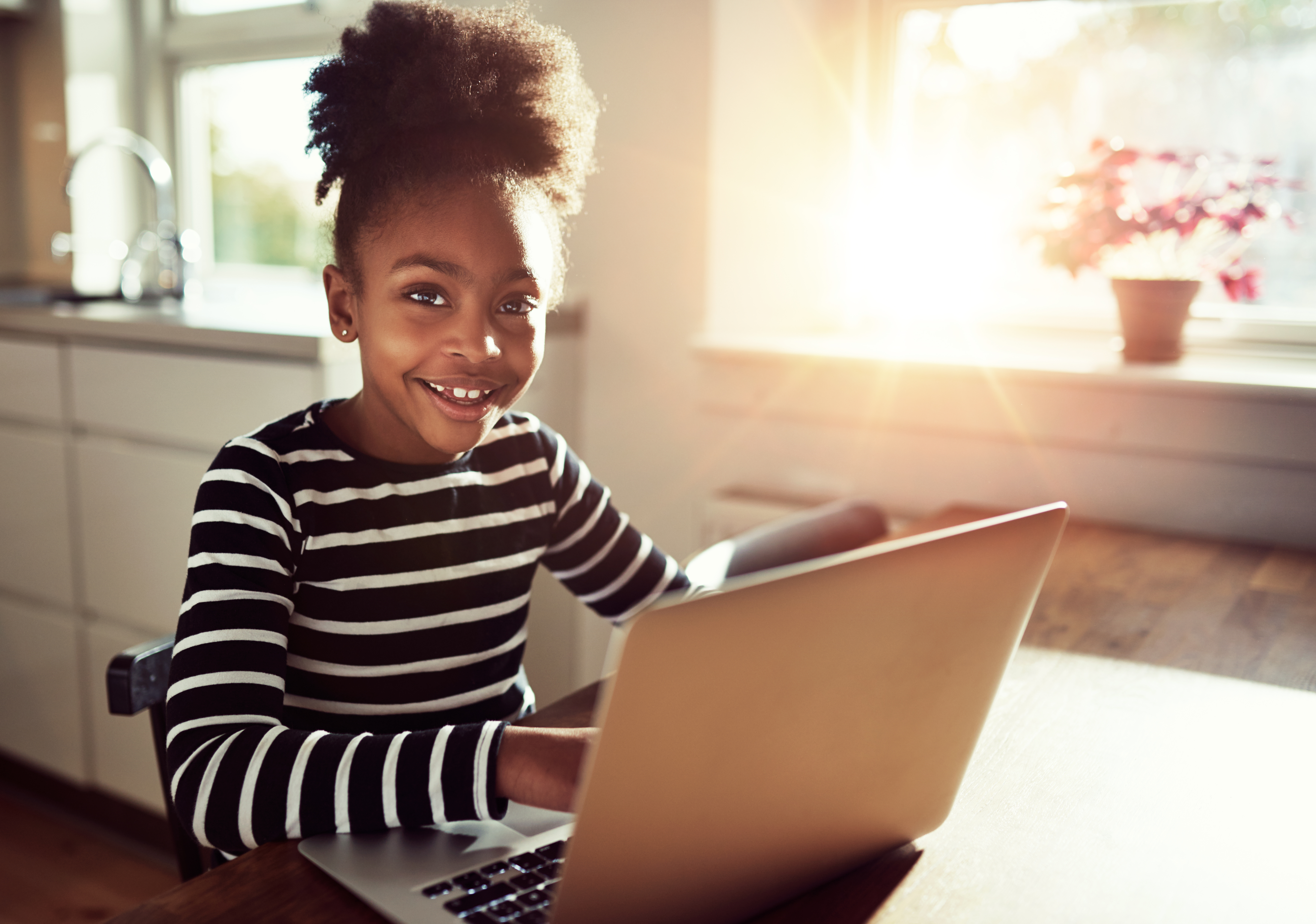 Child smiling at camera while using a laptop on a wooden table