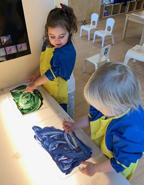 Two children in aprons painting with green and blue paint