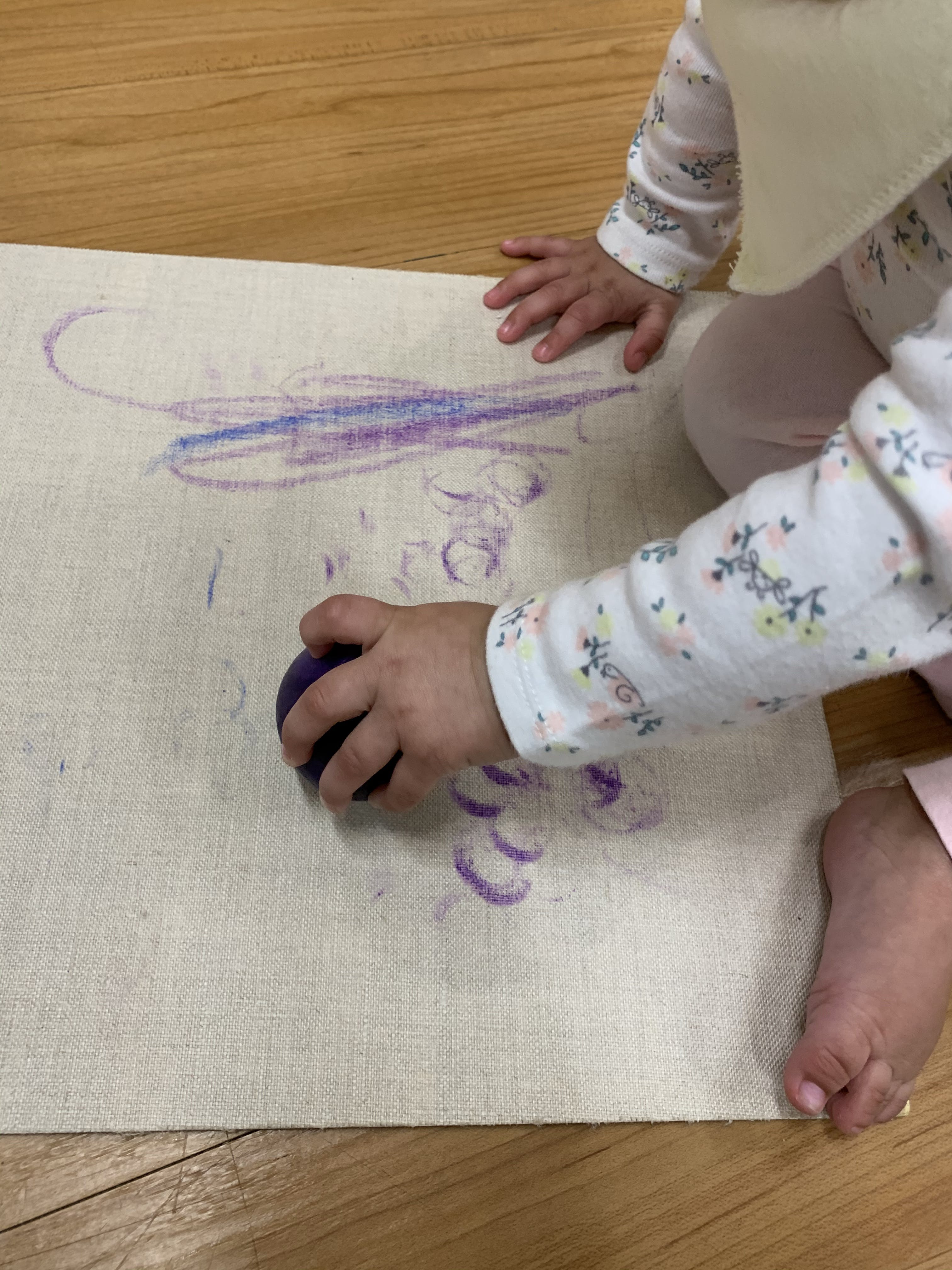Child drawing on a mat with a purple crayon