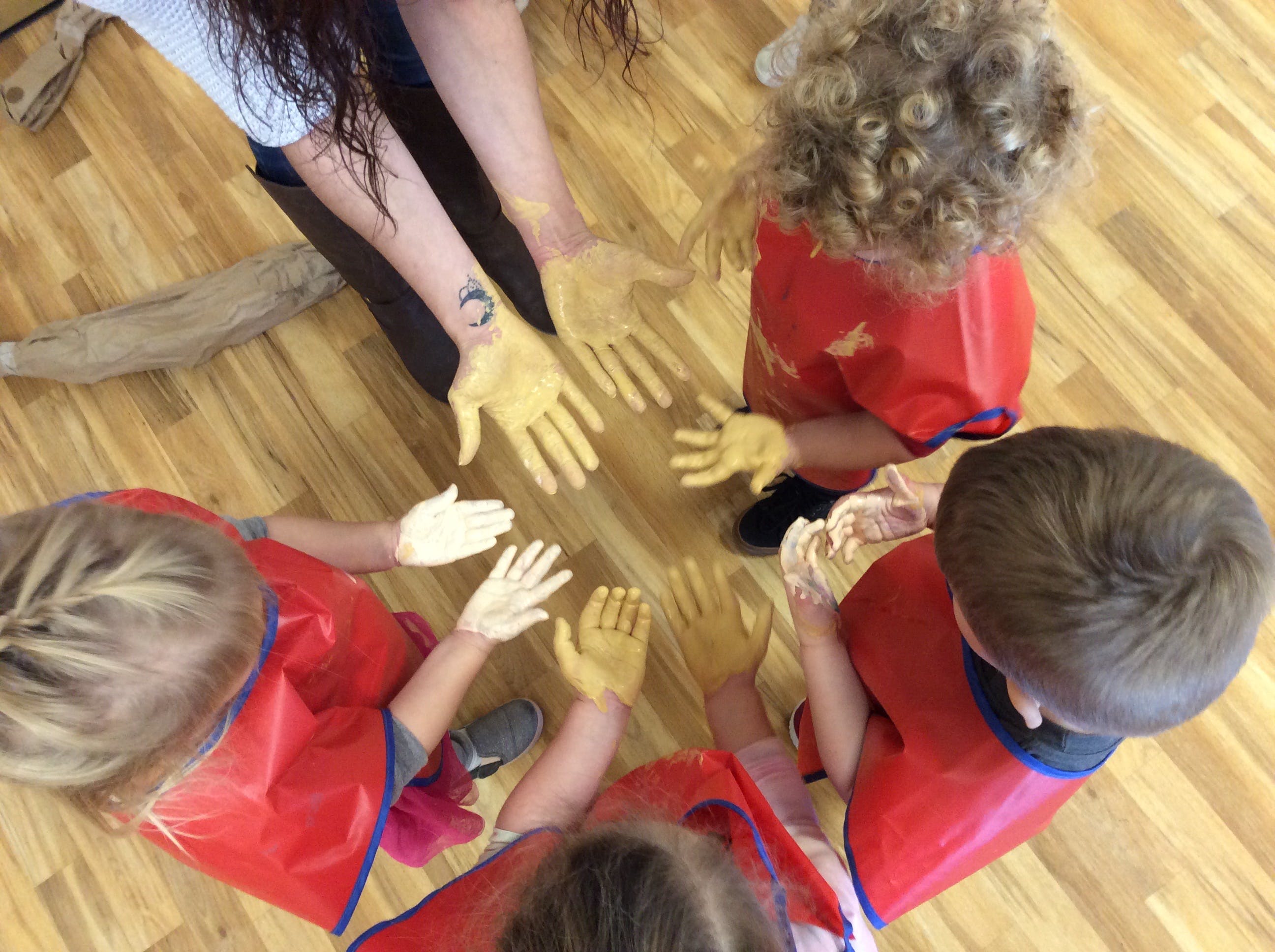 Person and children with painted hands on a wooden floor