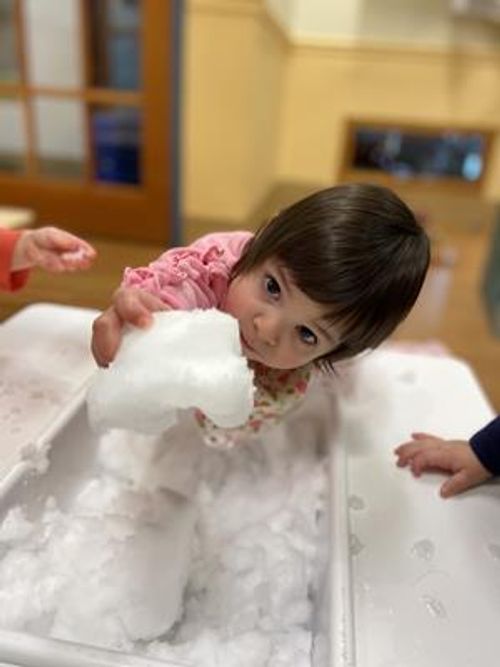 Child playing with white fluffy material in a bin