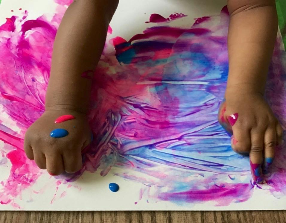 Child's hands finger painting with pink and blue paint