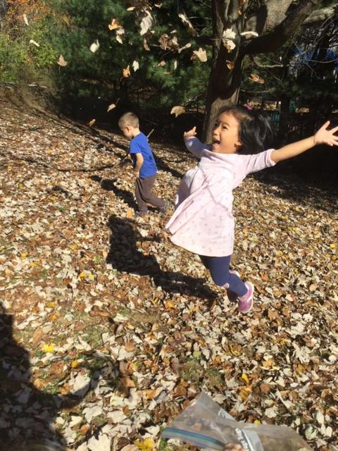 Child jumping with arms out, another child in background, leaves falling