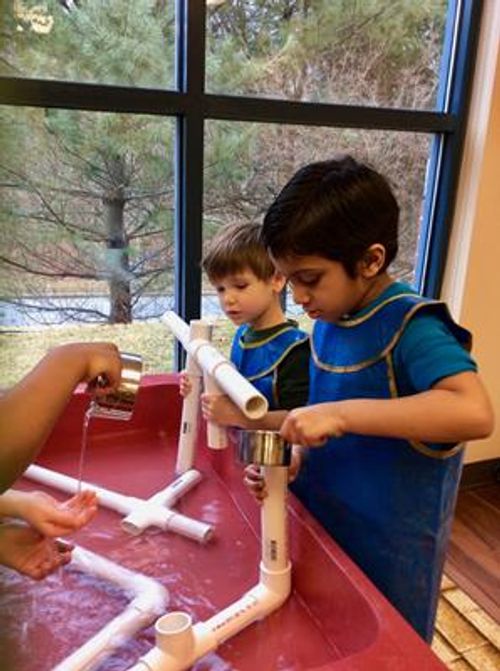 Children playing with water and PVC pipes in a red bin