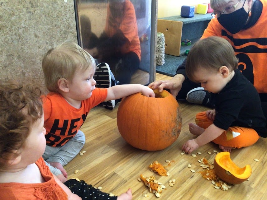 Three children and an adult carving a pumpkin on the floor
