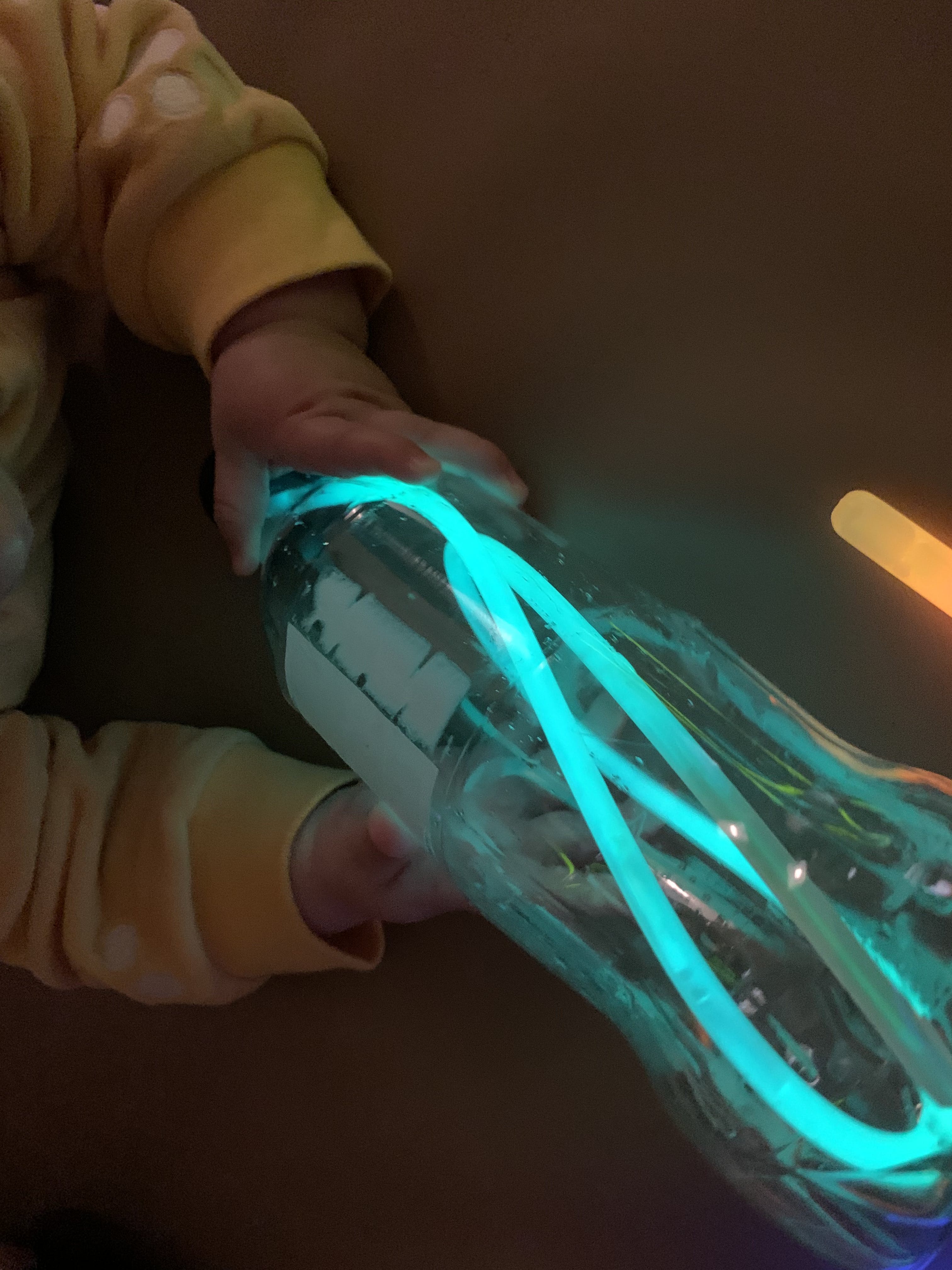 Child holding a plastic bottle with glowing blue light sticks inside