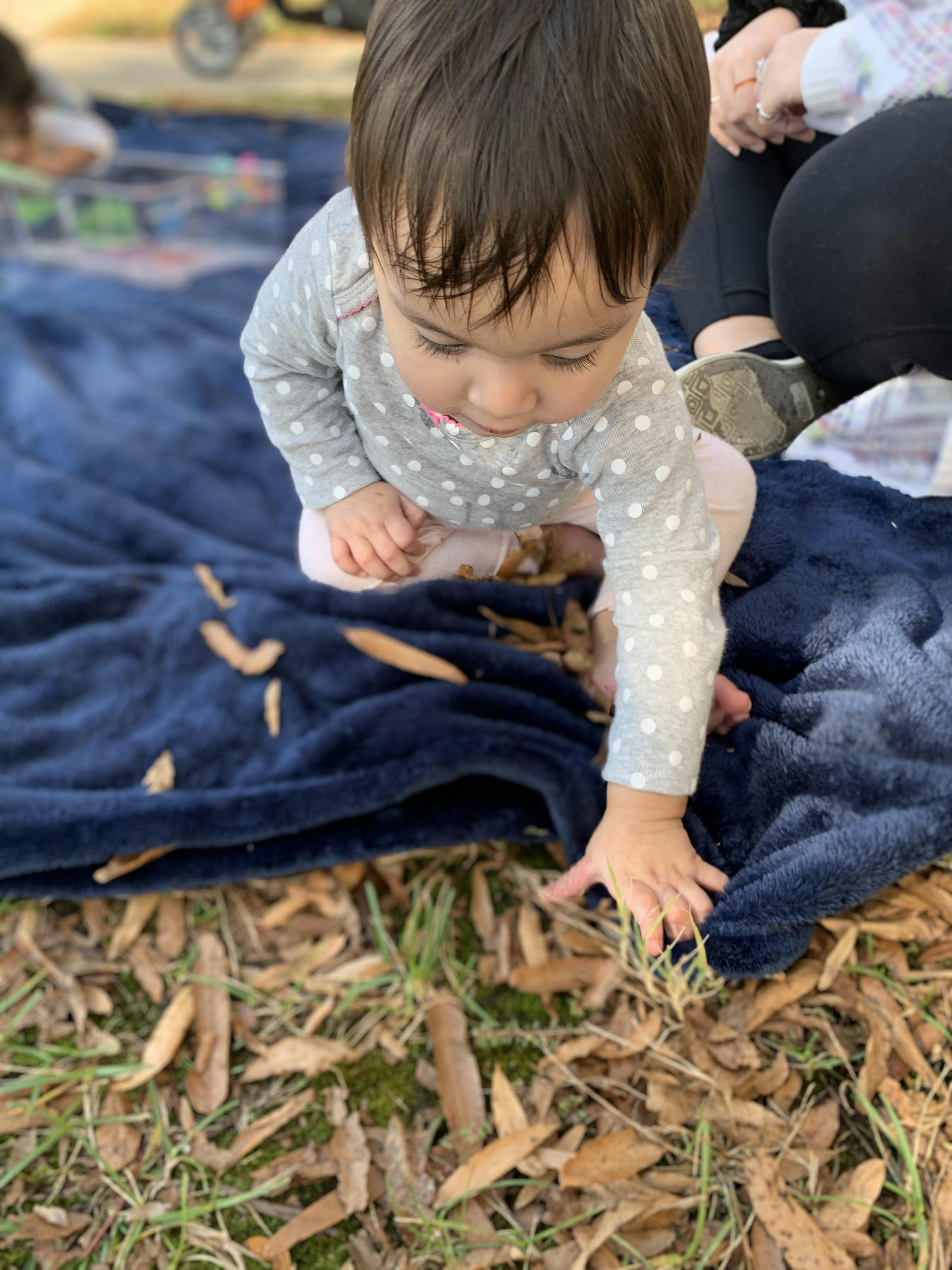 Child on a blanket reaching for leaves on the ground