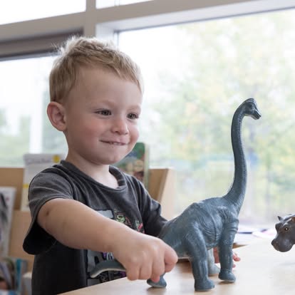 Child playing with a plastic dinosaur toy on a table