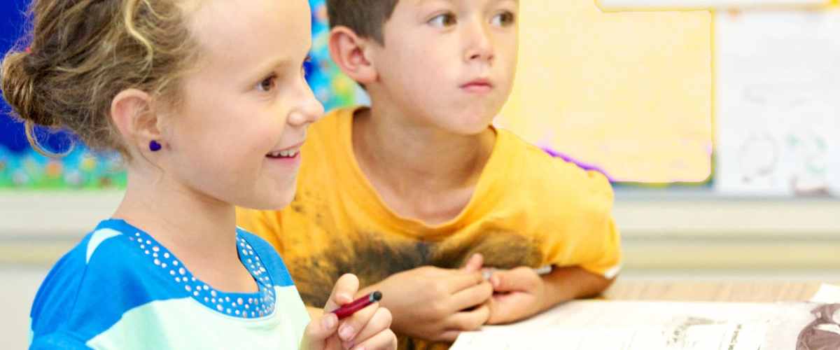 Two children in a classroom, one holding a crayon