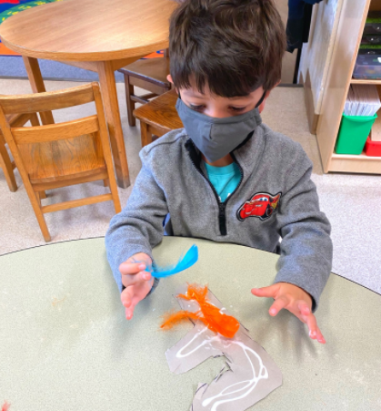 Child in a mask playing with orange and clear gel on a table