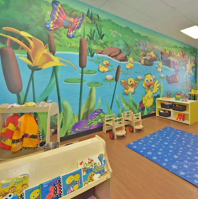 Playroom with a mural of a pond scene, small chairs, and a blue rug