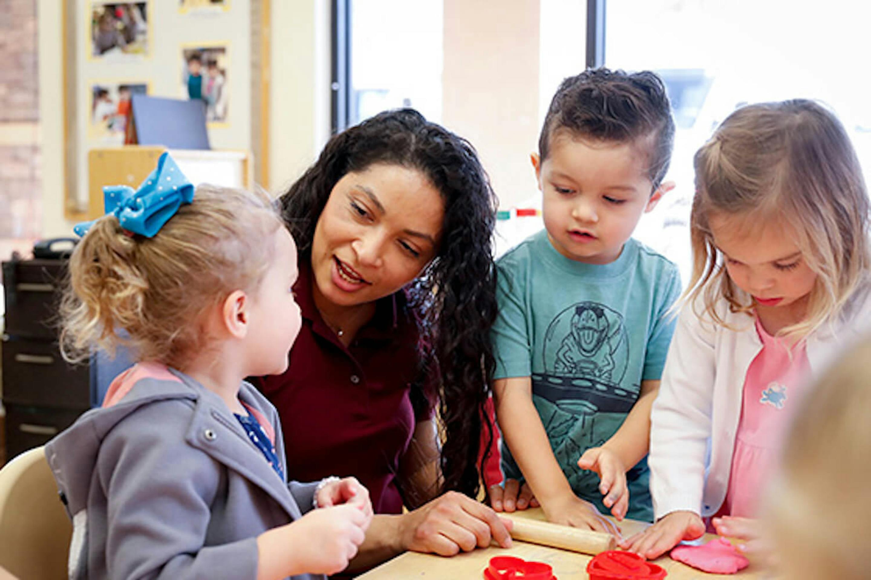 Person and three children playing with modeling clay in a classroom