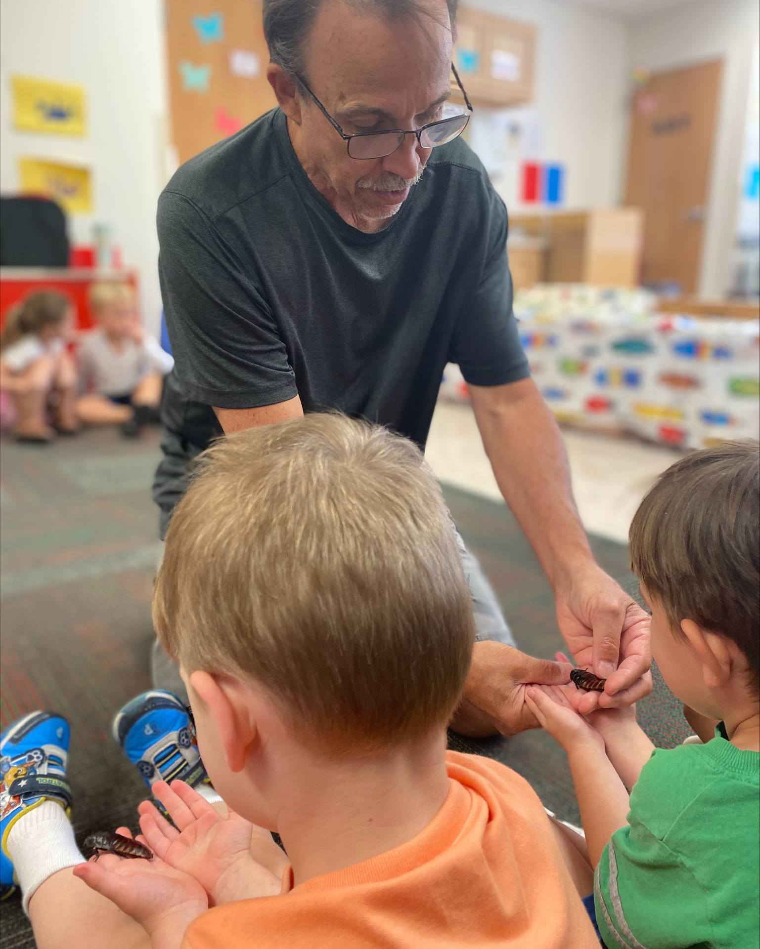Adult showing small object to two children in a classroom