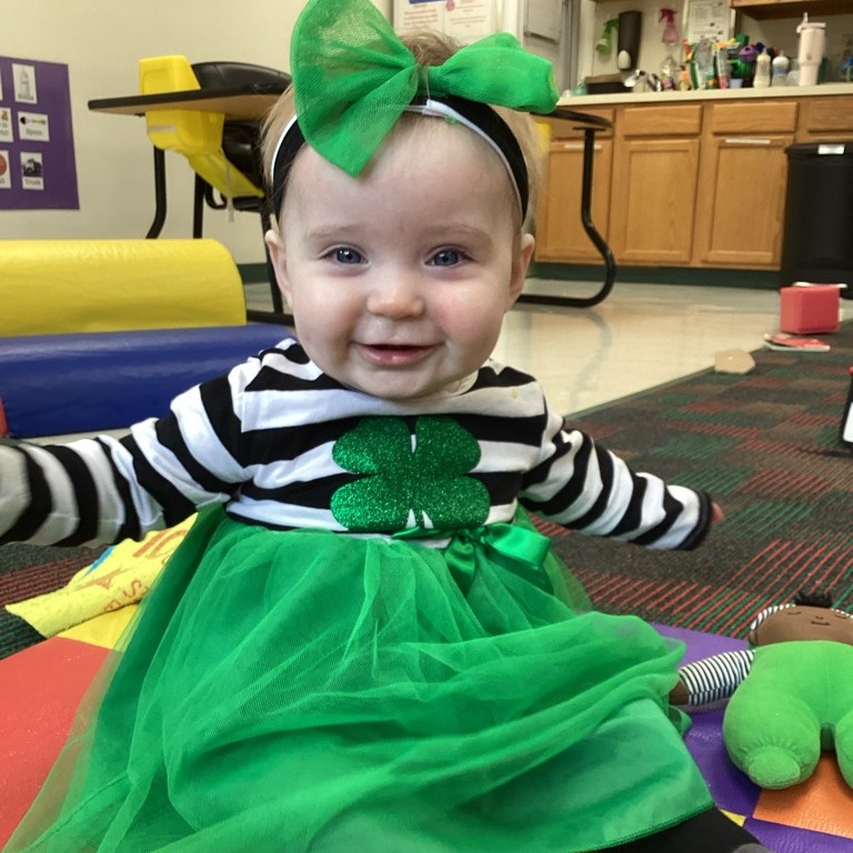 Child in striped shirt and green skirt with a shamrock and bow