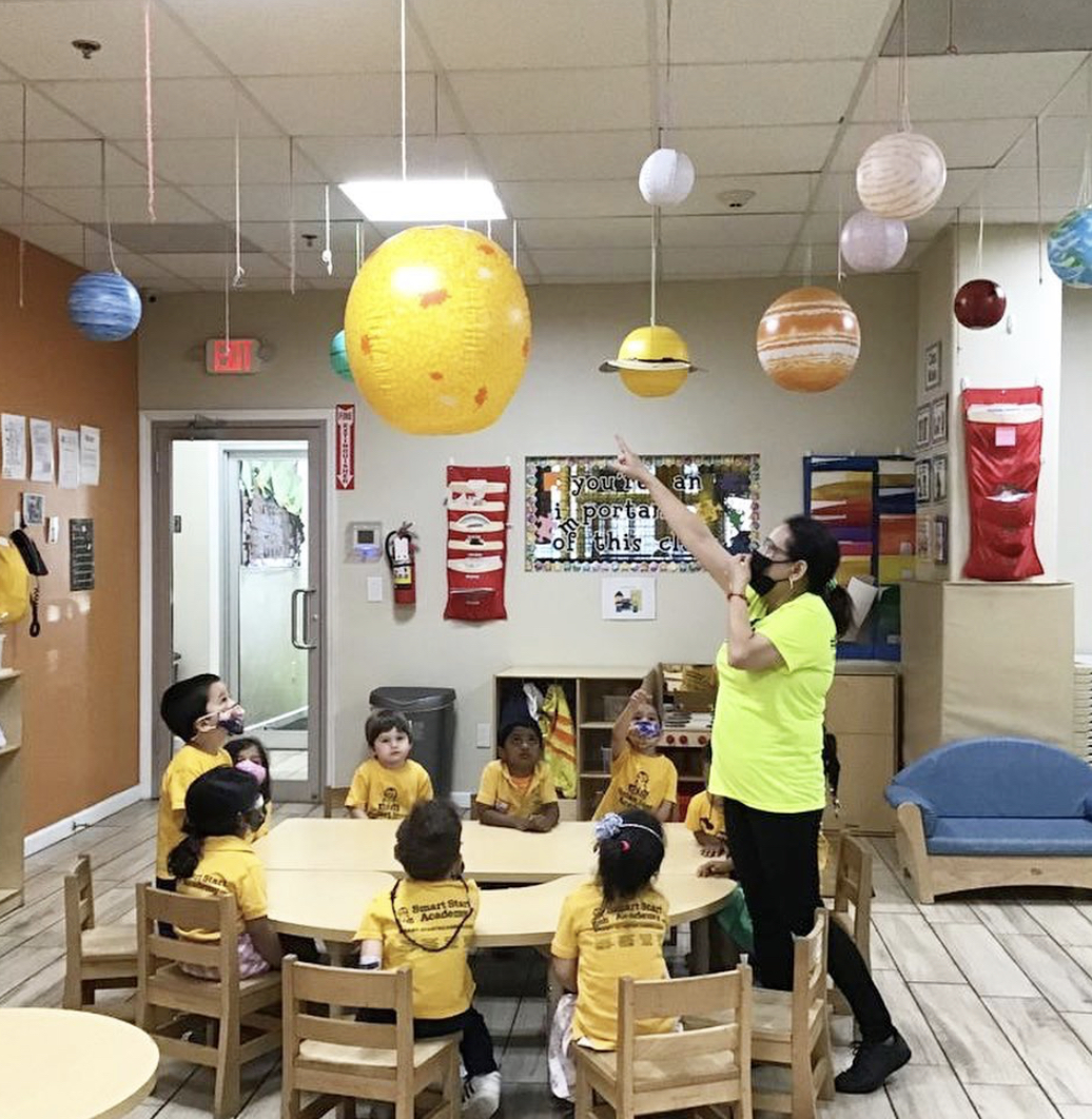Person teaching children in a classroom with hanging planet decorations