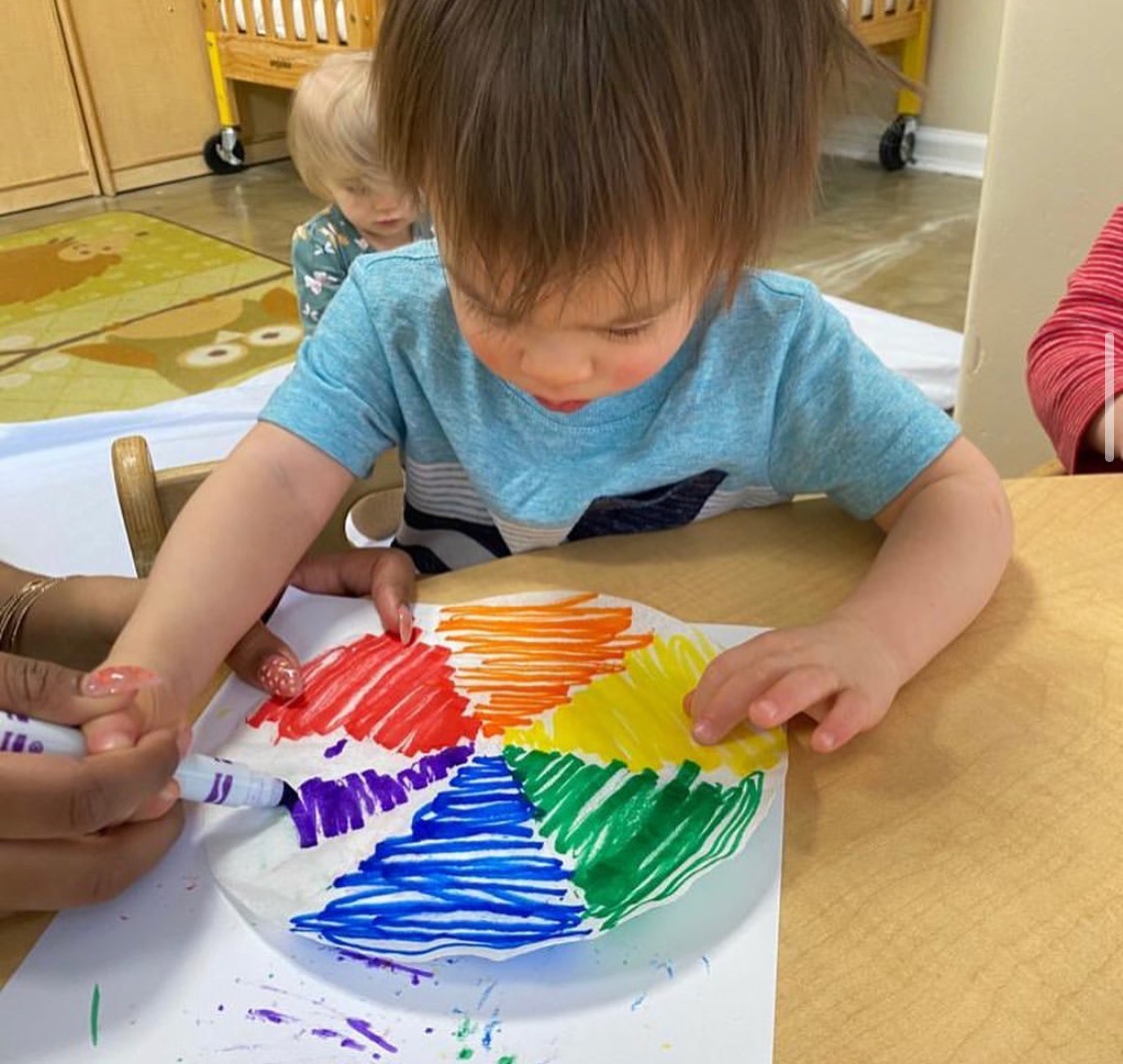 Child coloring a paper plate with rainbow colors