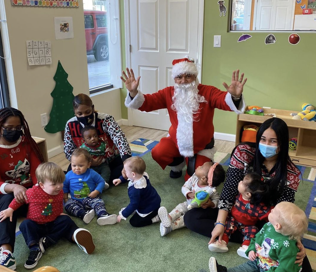 Santa Claus with hands raised, surrounded by adults and children