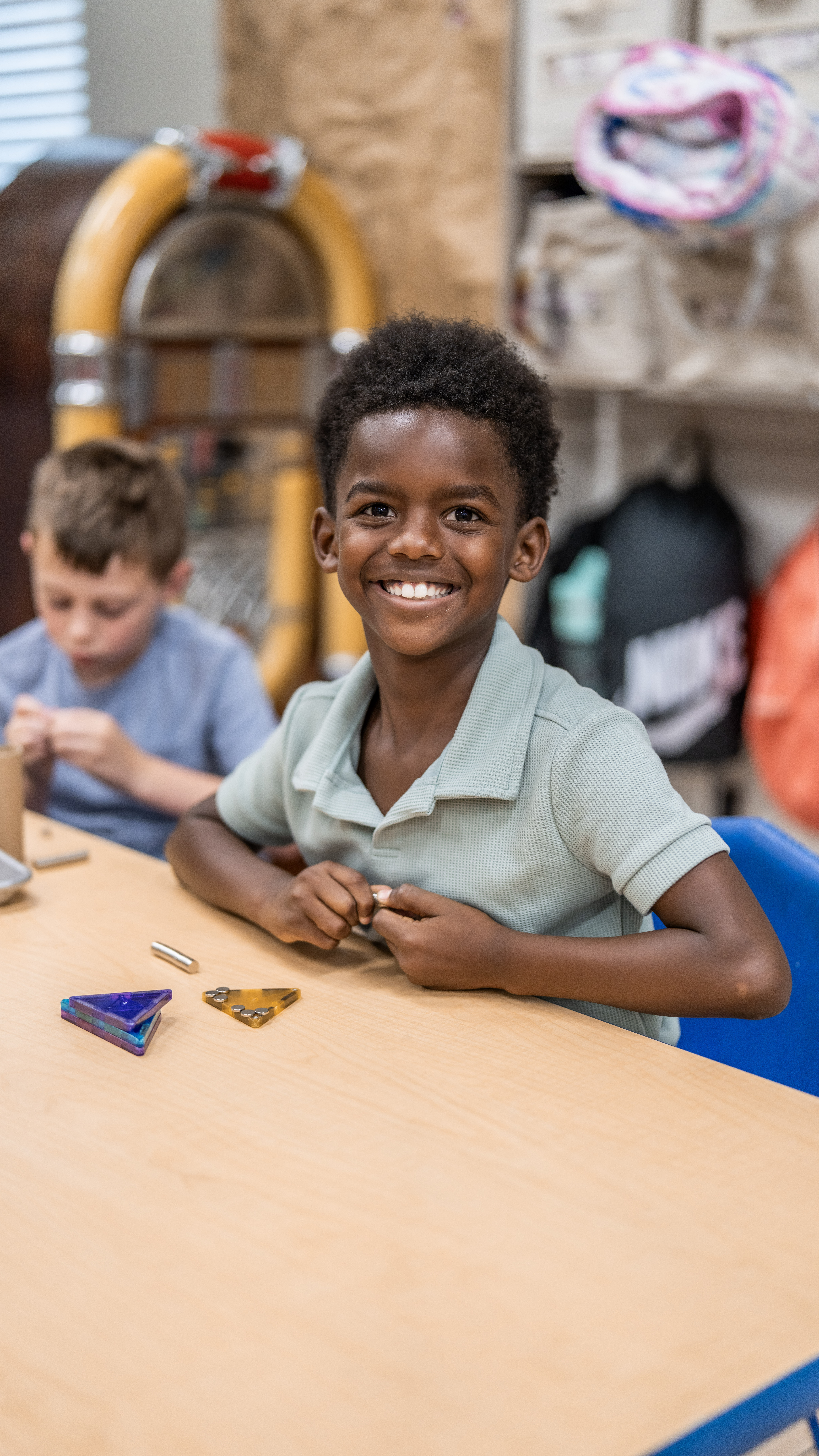 Child smiling while playing with magnetic building pieces at a table