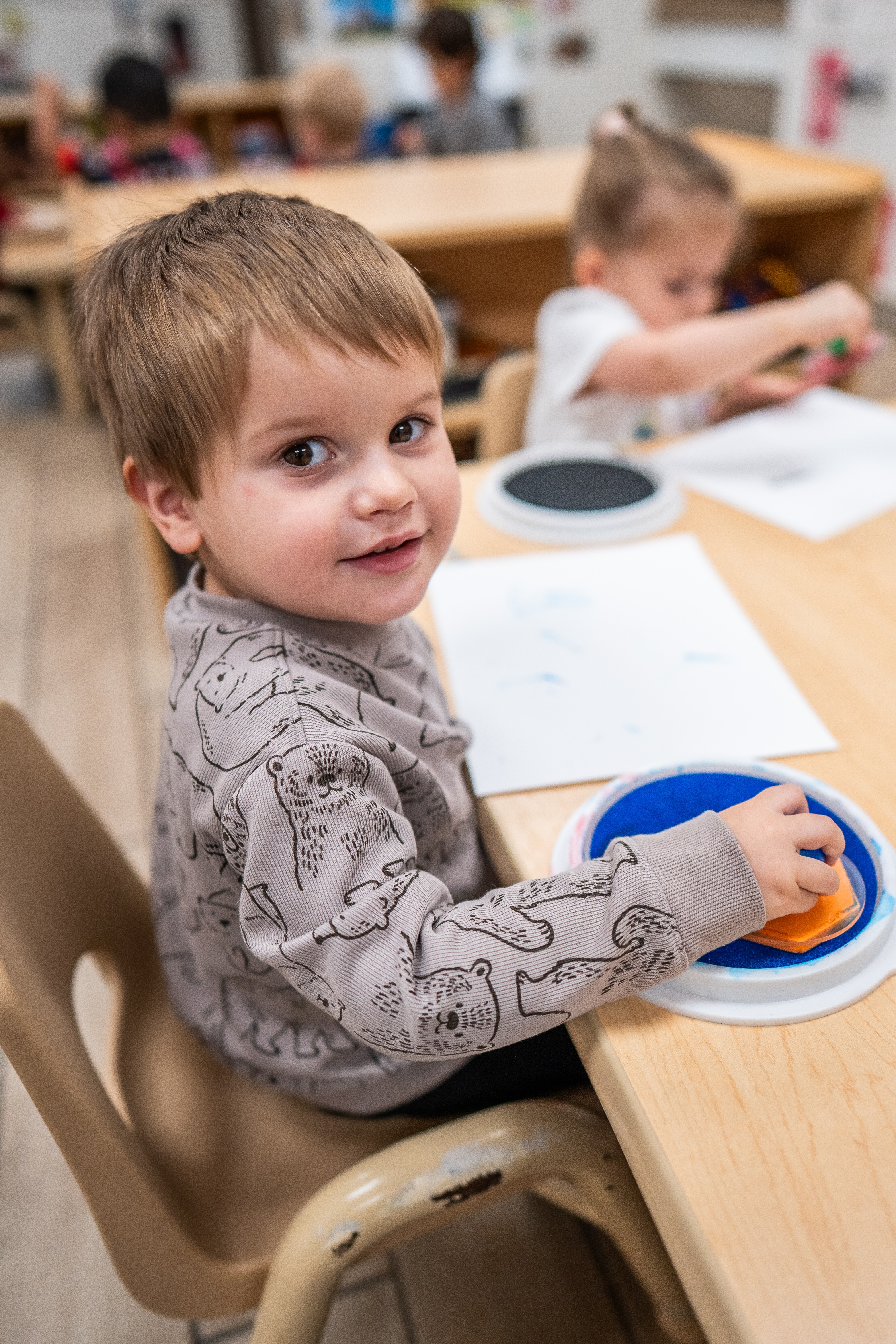 Child sitting at a table using a stamp pad in a classroom