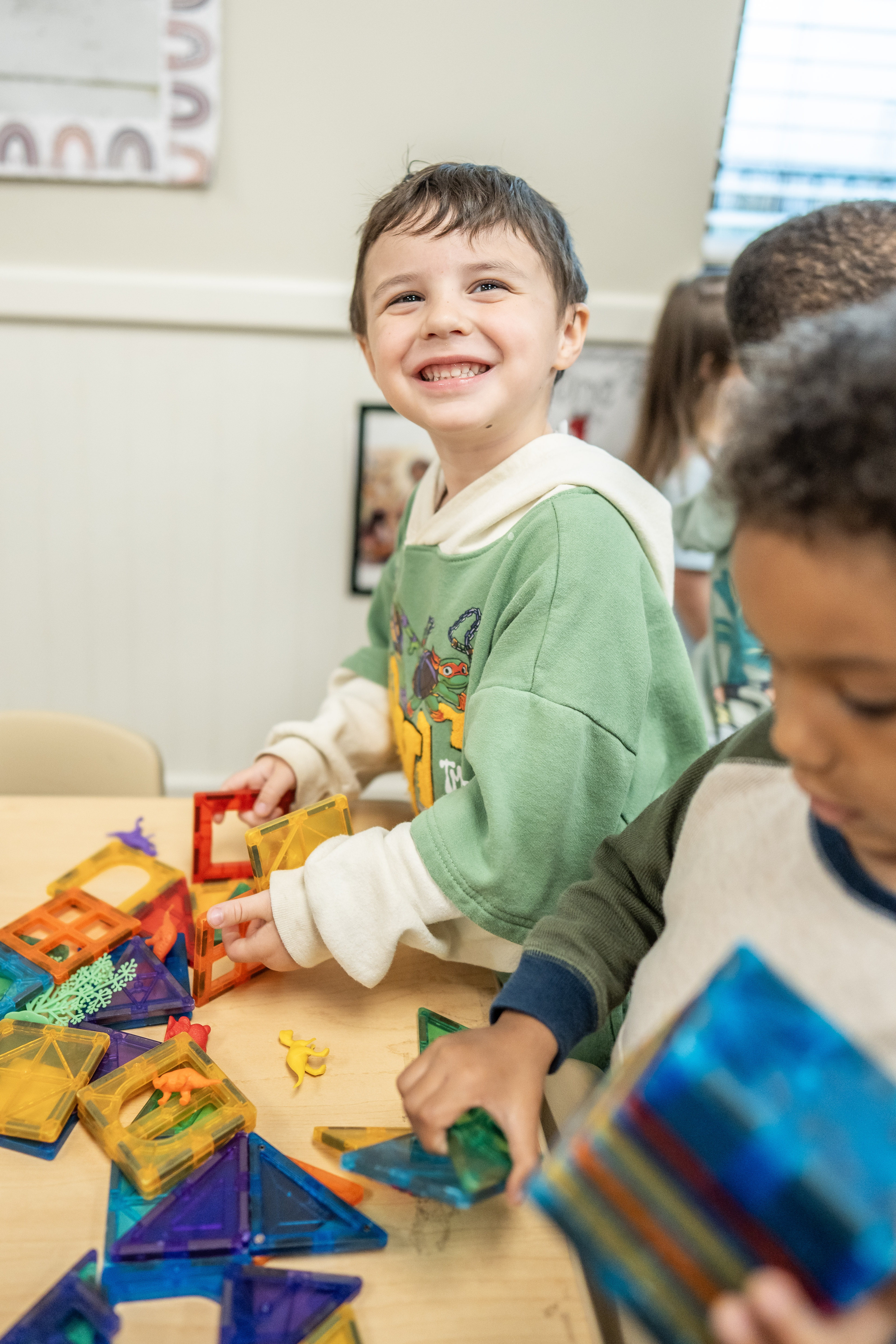 Children playing with colorful magnetic building tiles on a table