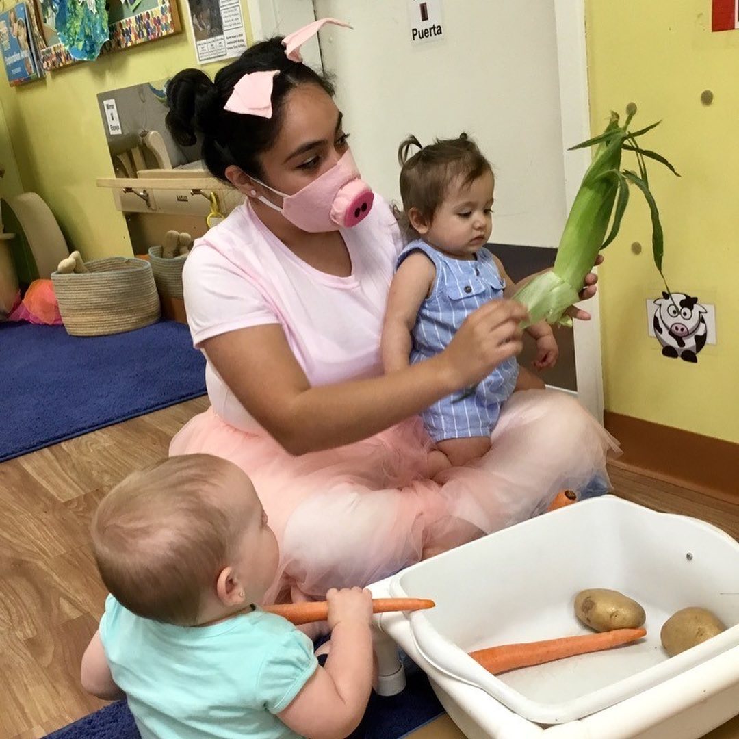 Person in pig mask holding a child, another child with carrots and vegetables