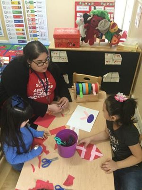Adult and two children doing crafts at a table in a classroom