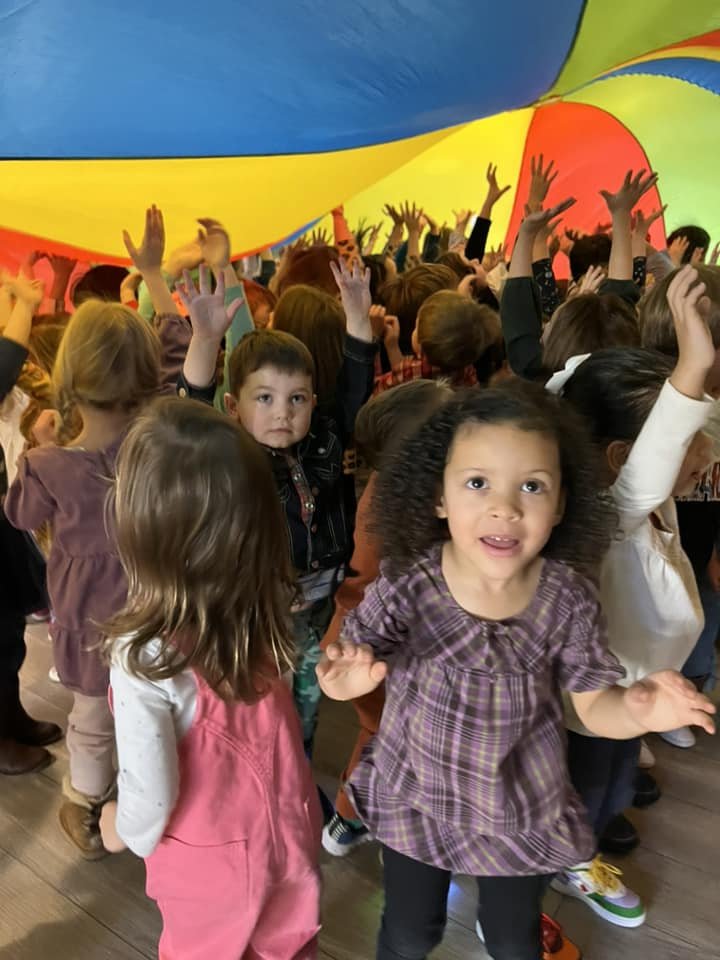 Children playing under a colorful parachute with hands raised