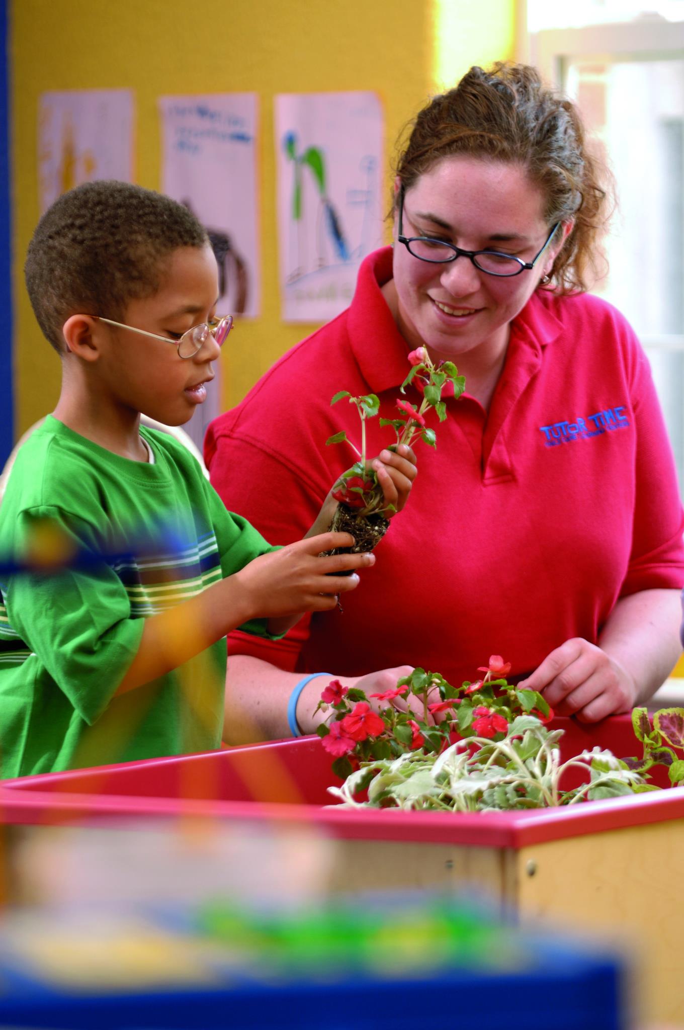 Person and child planting flowers in a classroom