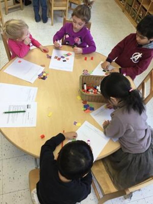 Children sitting at a round table with papers and colorful shapes