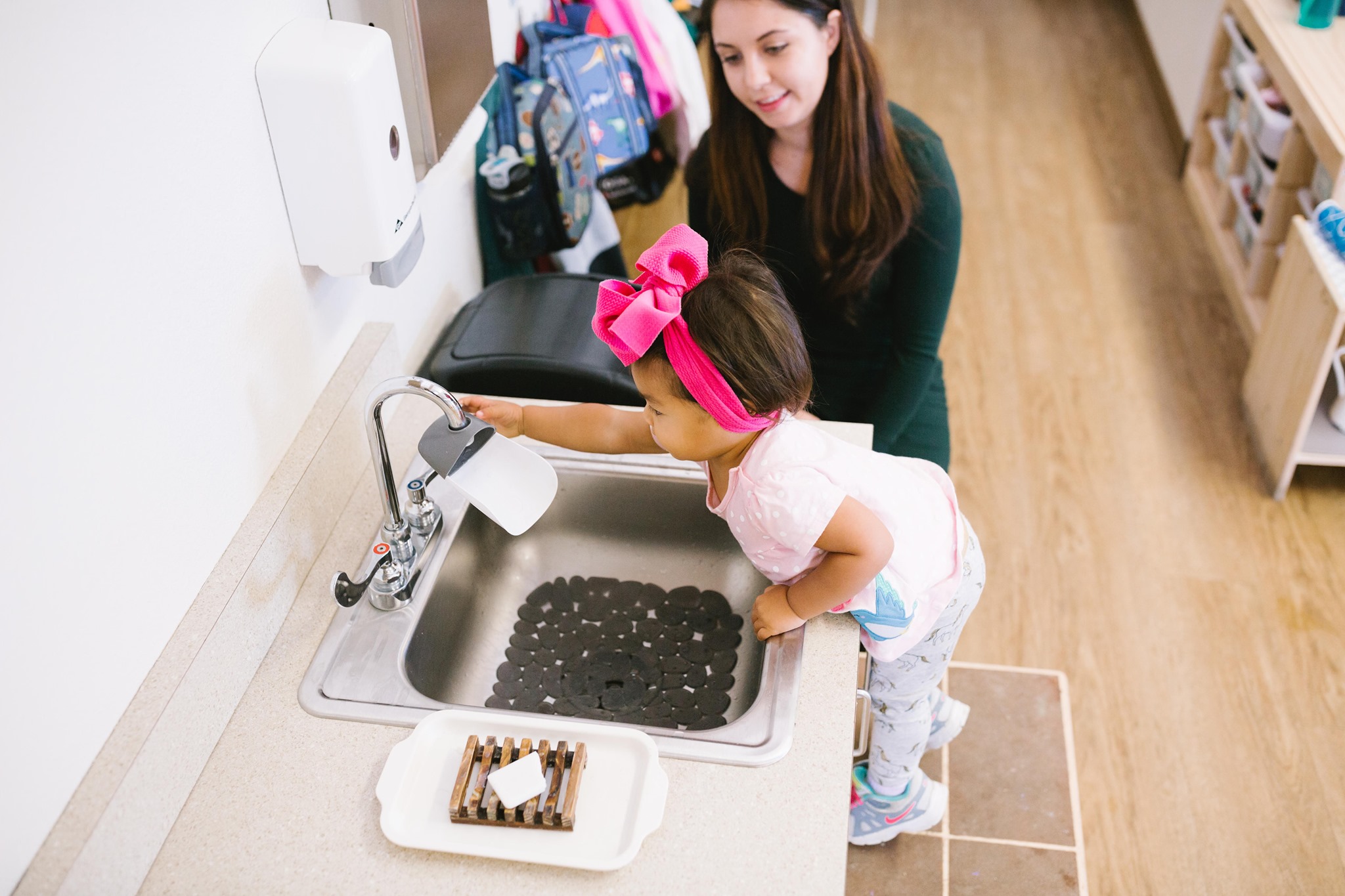 Adult and child at a sink, child holding a cup under the faucet