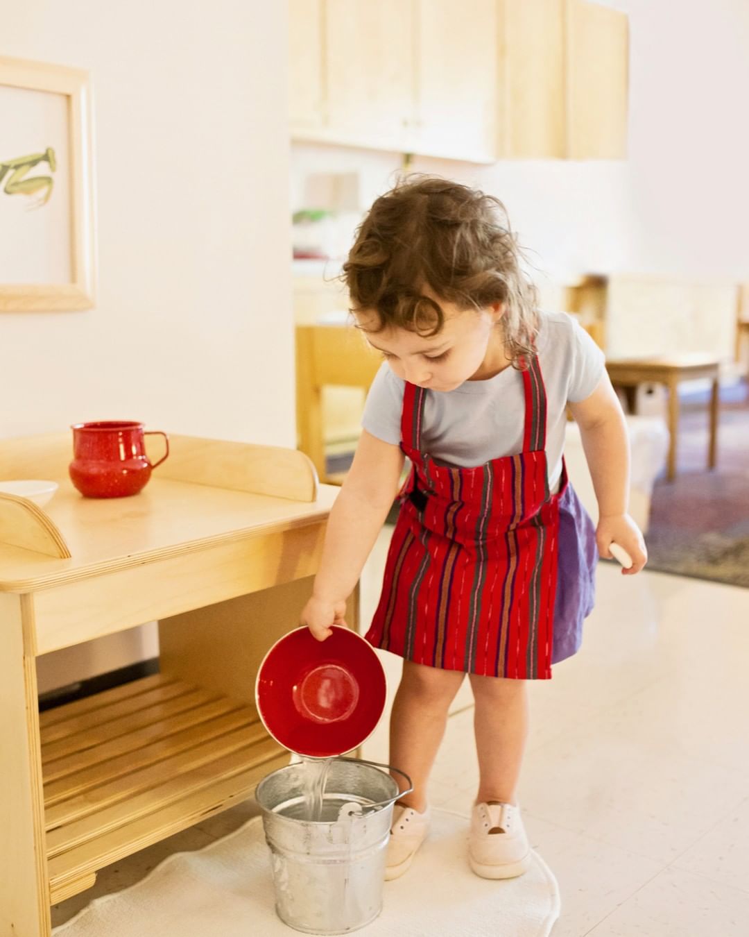 Child in an apron holding a red plate over a bucket