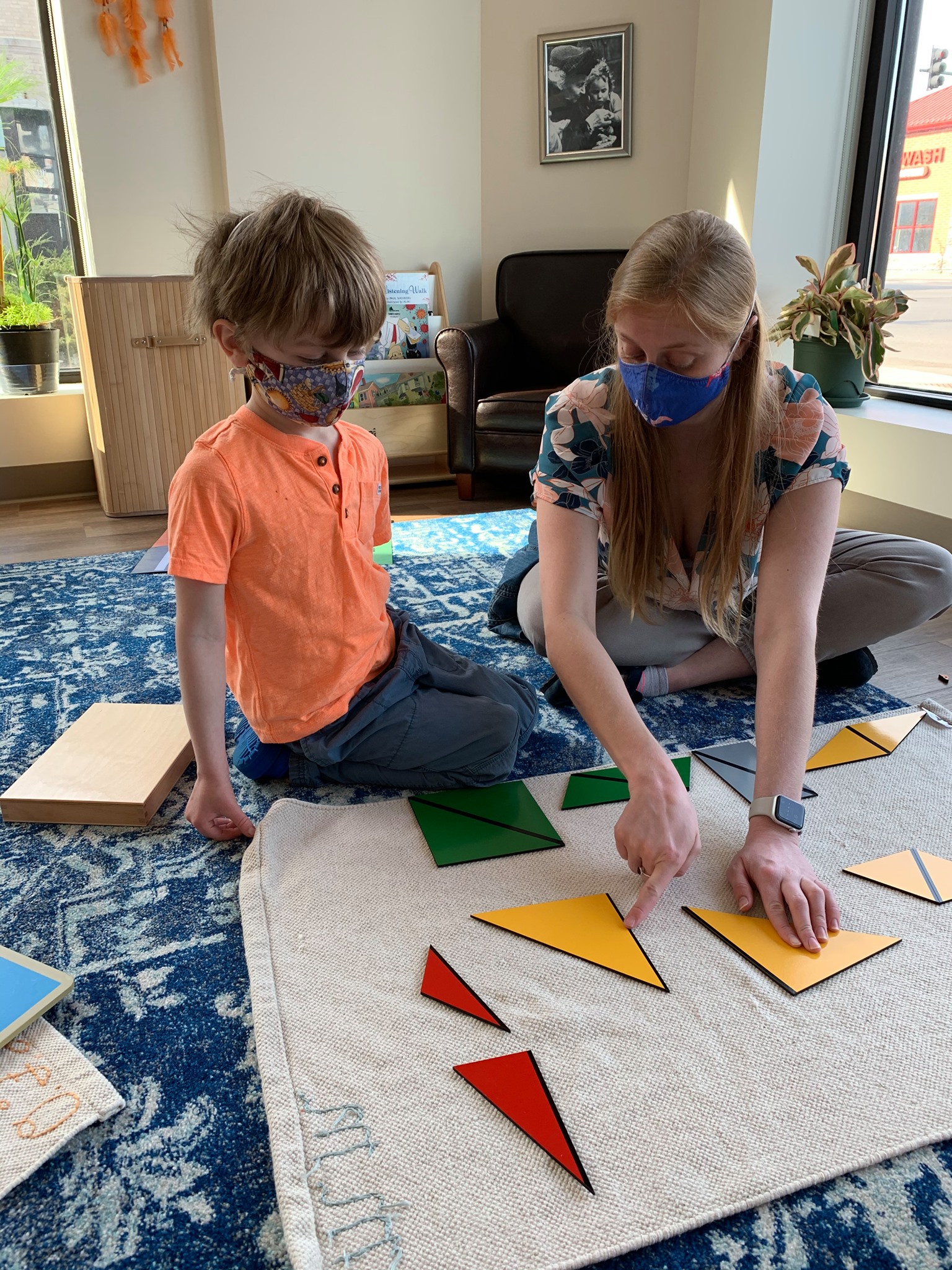 Adult and child in masks arranging geometric shapes on a mat
