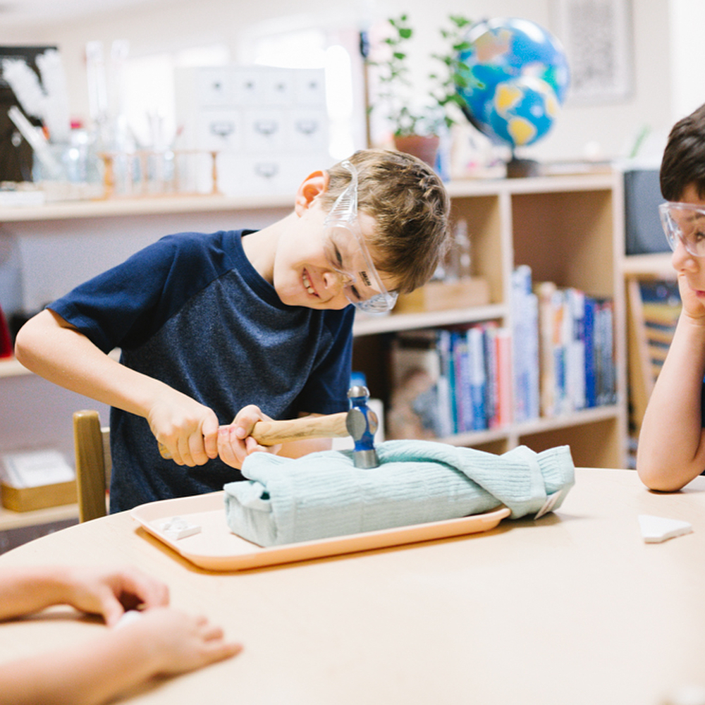 Child in safety glasses hammering an object in a classroom
