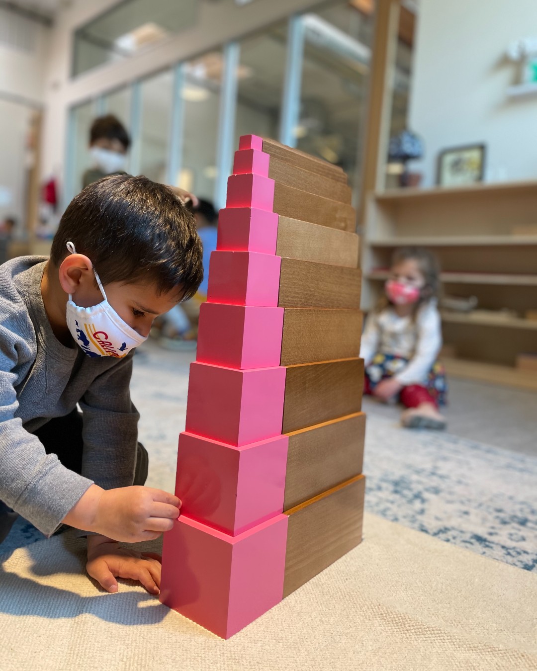Child in mask building a tower with pink and brown blocks
