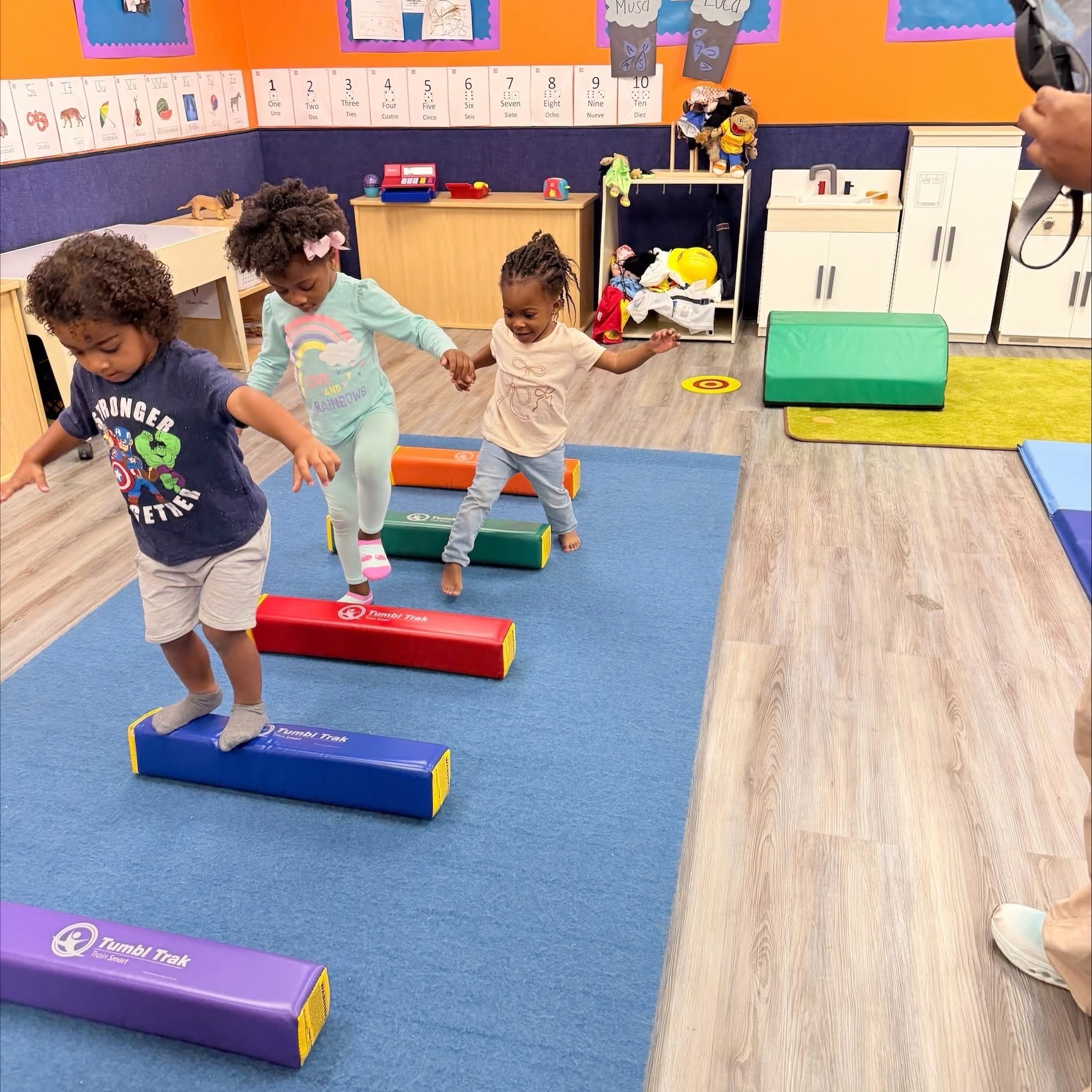 Three children walking across a line of foam balance beams in a classroom