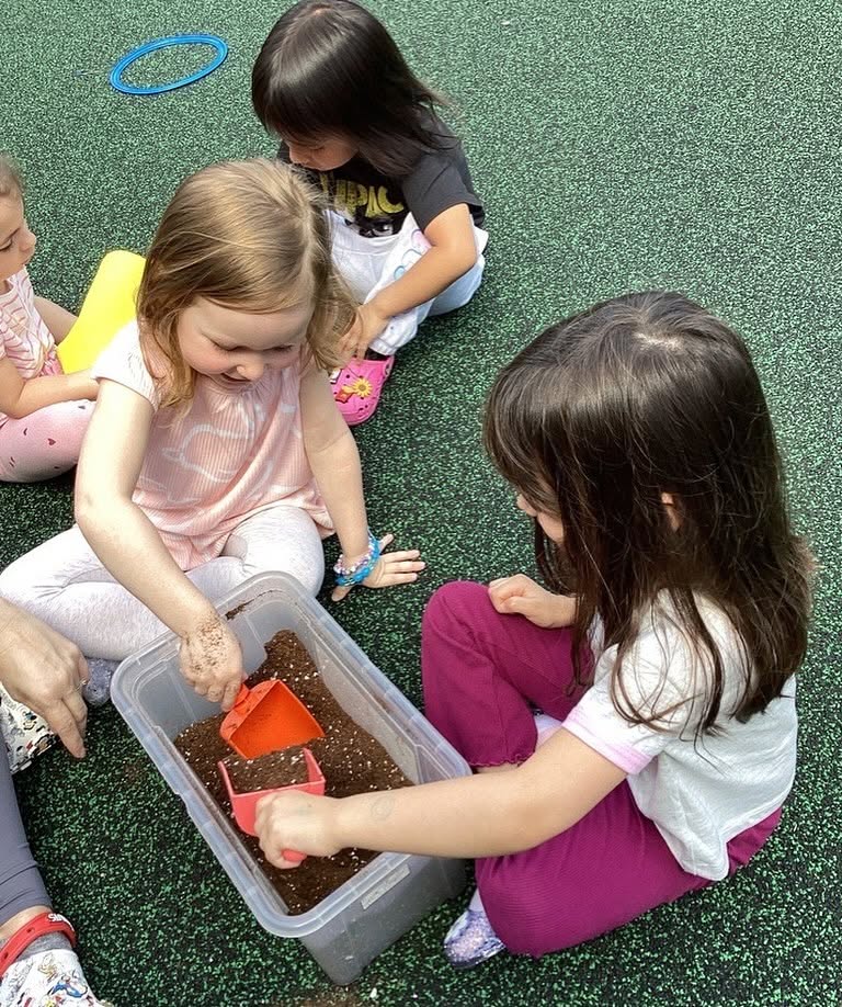 Children playing with plastic scoops in a bin of soil