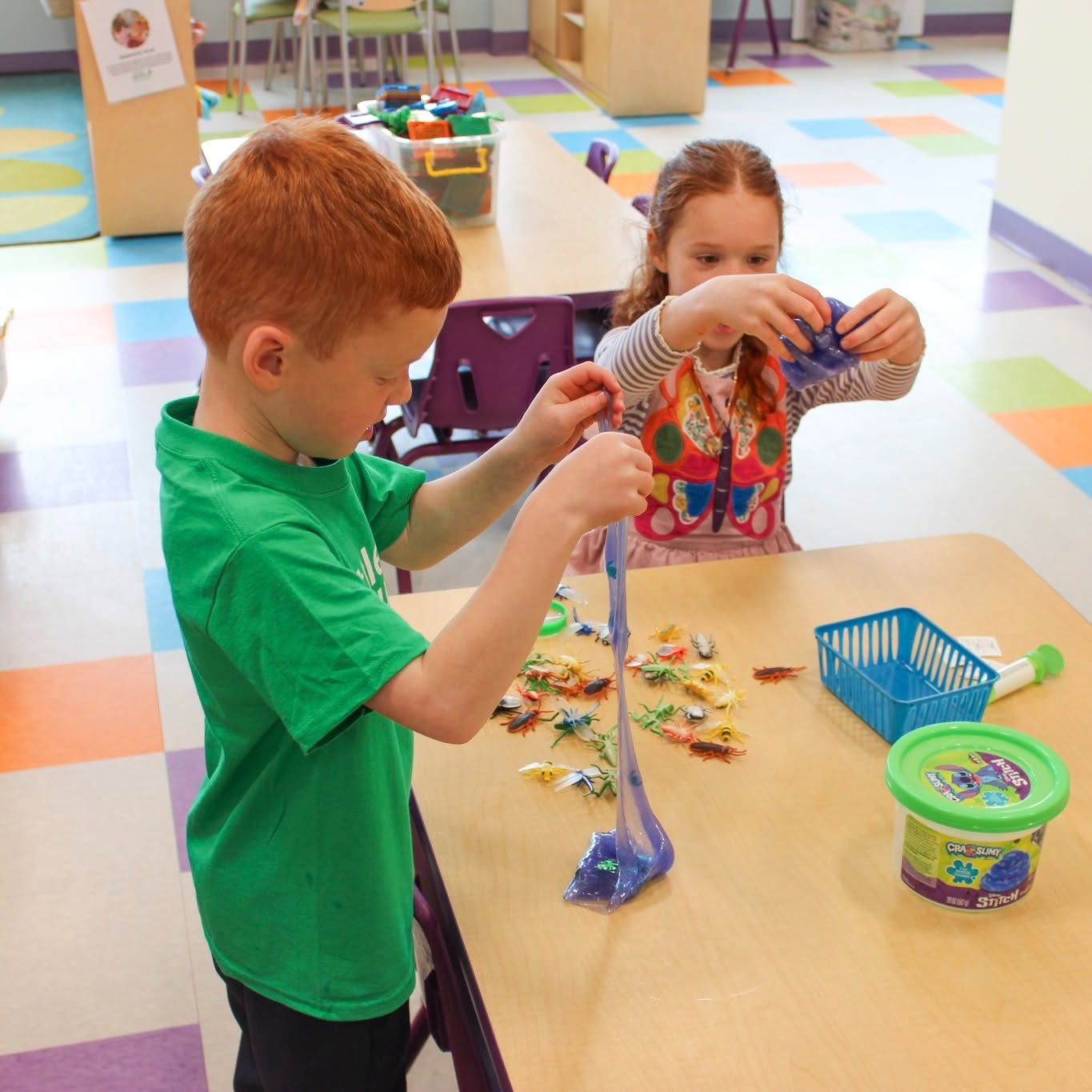 Two children playing with blue slime and plastic insect toys at a table