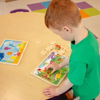 Child assembling a dinosaur jigsaw puzzle at a table