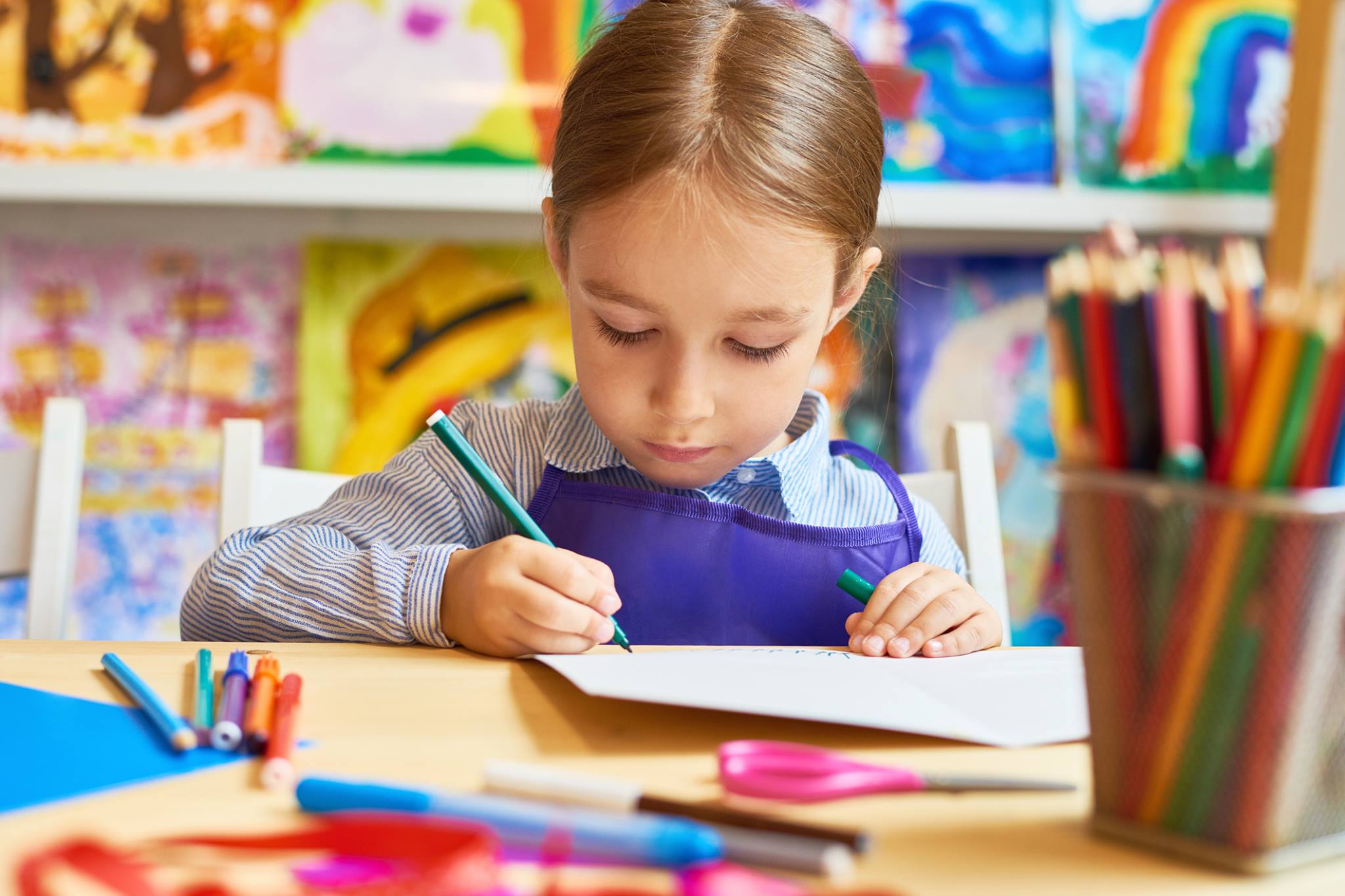 Child drawing on paper with a green pencil