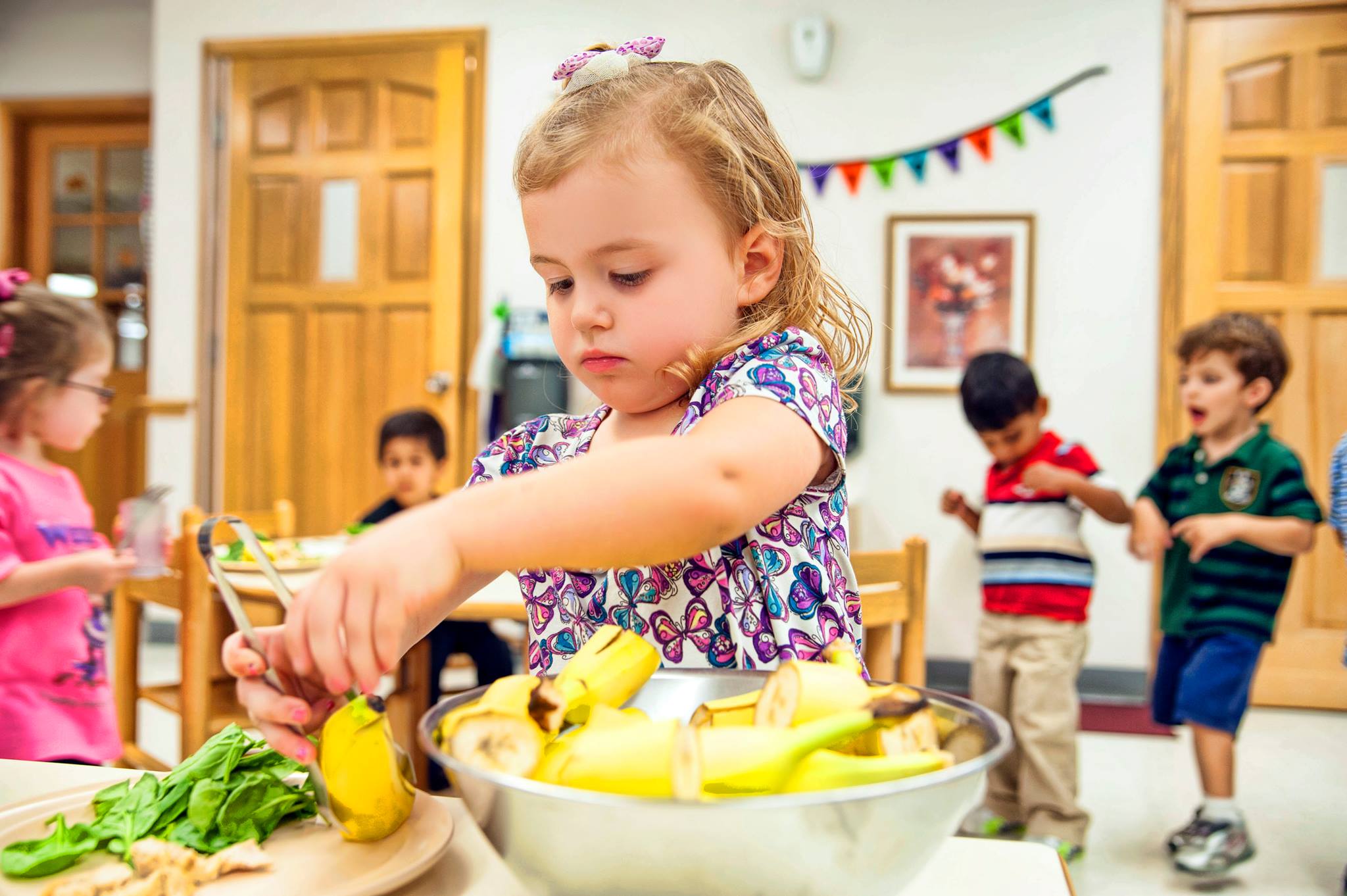 Child peeling a banana in a bowl with other children in the background