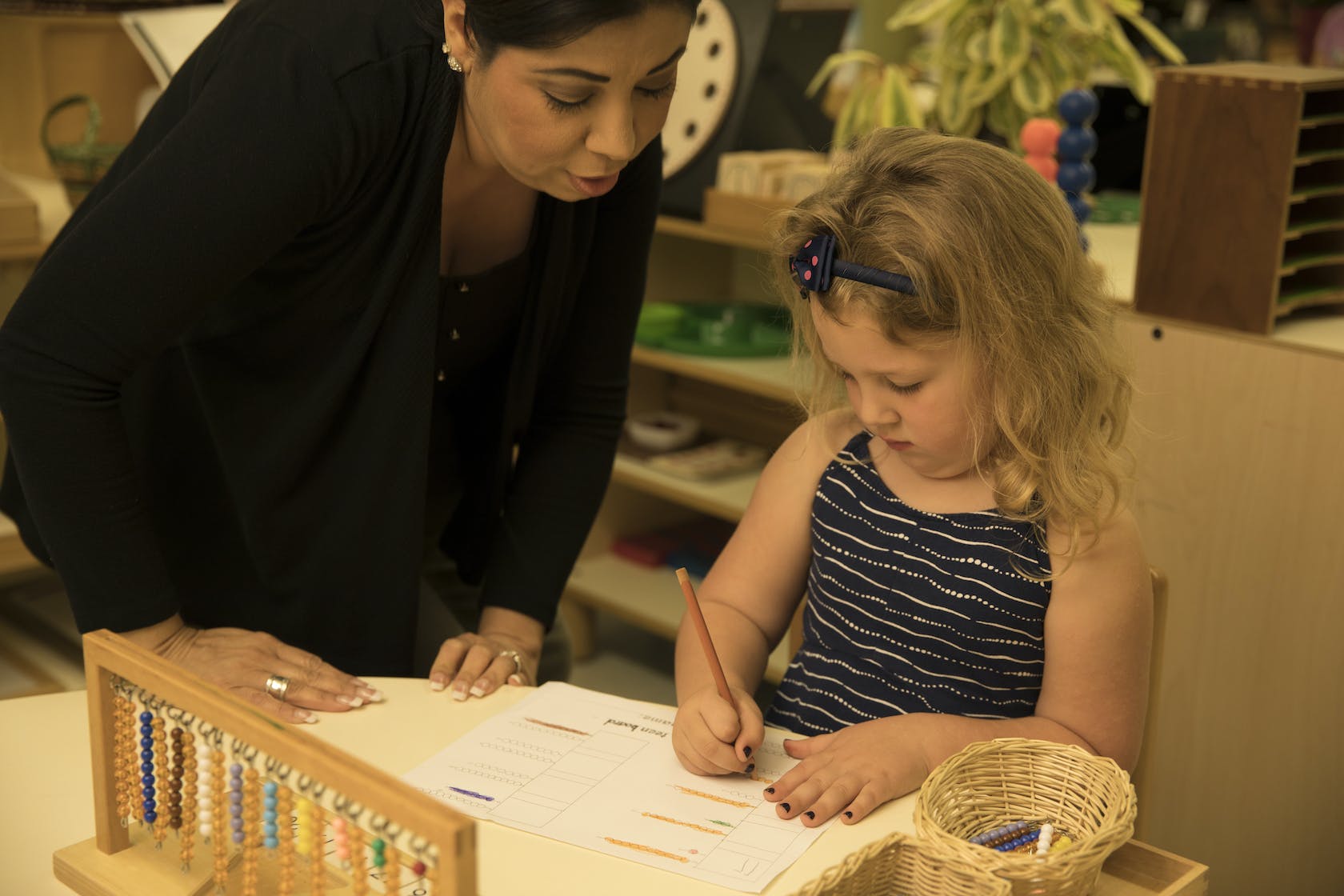 Adult and child writing at a table in a classroom