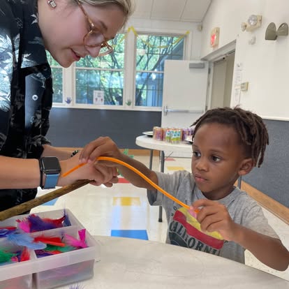 Person helping a child with an orange craft string