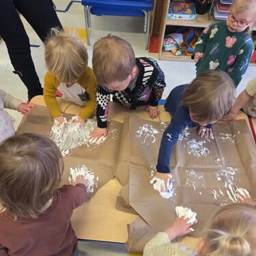 Children finger painting with white paint on brown paper