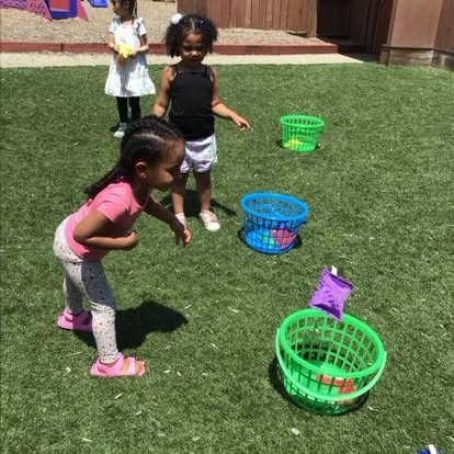 Three children playing with baskets on a grassy area