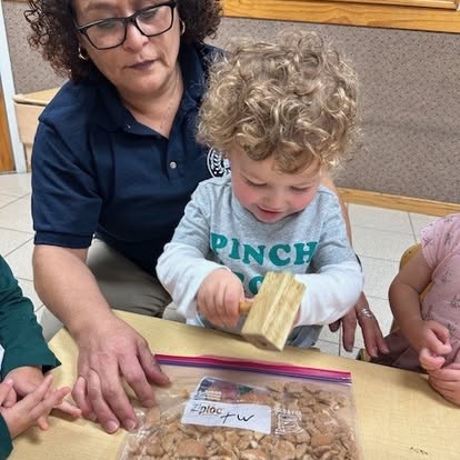 Person and child using a wooden mallet to crush contents in a plastic bag