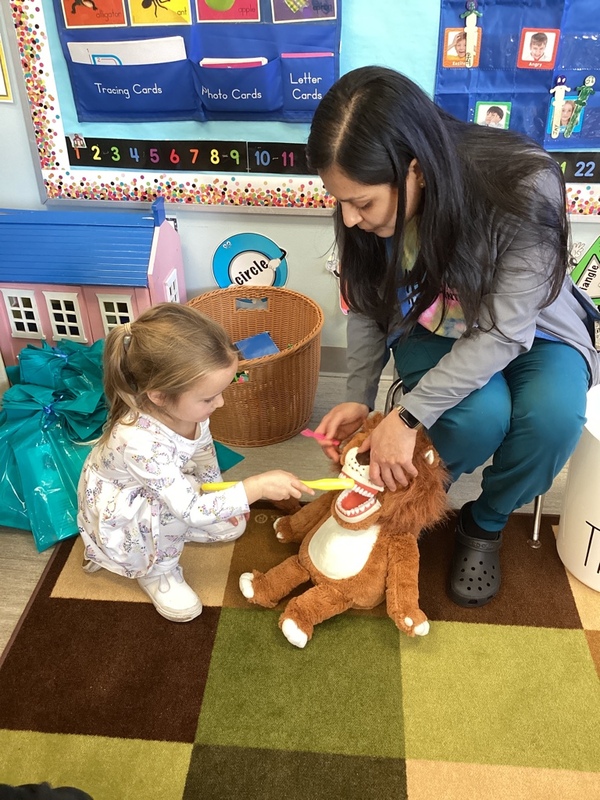 Adult and child brushing teeth of a stuffed animal